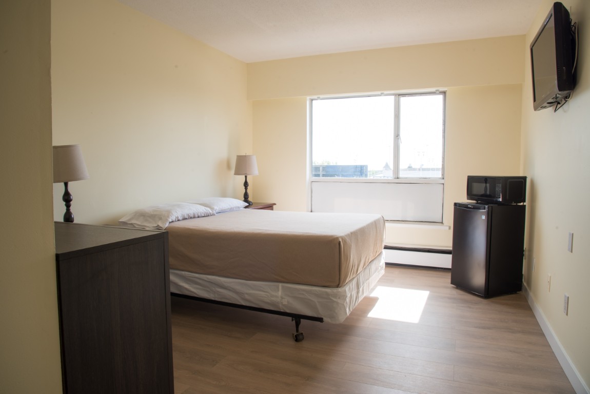 Bright studio with bed, side tables, dresser, mounted TV, and microfridge