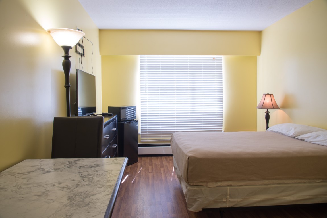 Single occupancy furnished studio with bed, dresser, microfridge, and wall-mounted TV