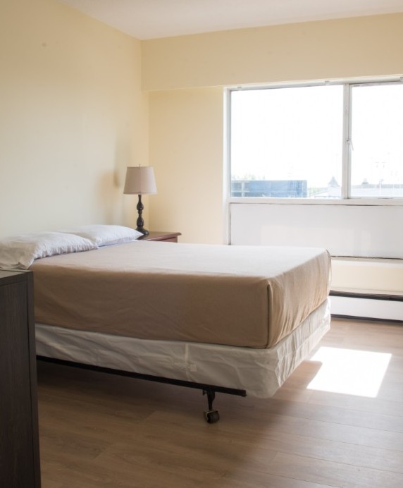 Furnished studio bedroom with bed, floor lamp, and window with city view
